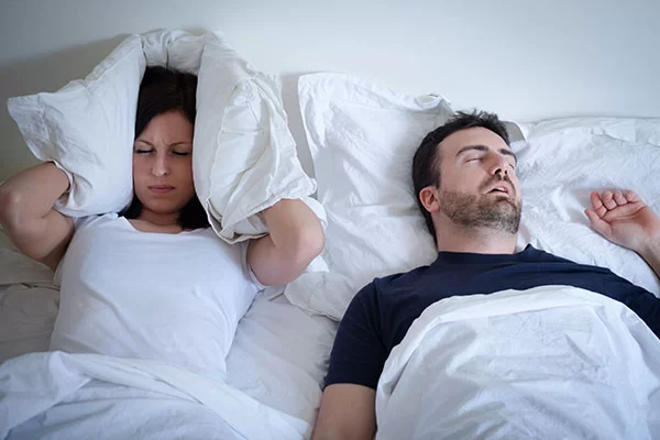 woman covering her ears from her bed partner's loud snoring